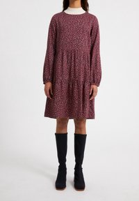 Robe bordeaux à manches longues, en tissu texturé, avec un col blanc et un motif de feuilles claires dispersées ; complétée par des bottes noires à mi-mollet.