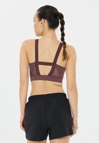 Bordeaux sportbeha met brede banden en gaaspanelen, gecombineerd met zwarte sportshorts met een elastische tailleband.