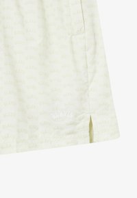 Chemise jaune clair arborant un motif répété "BLKVIS" sur l'ensemble, avec une fente latérale et un logo brodé sur l'ourlet.