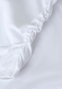 Hvidt stof med en samlet søm, glat tekstur og en subtil glans. Har bløde draperinger og en afslappet pasform omkring kanterne.