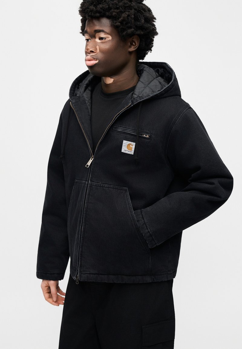 Veste en jean noire avec fermeture éclair et capuche. Comprend une poche avant et une poche poitrine, une doublure matelassée et une étiquette logo sur la poitrine.