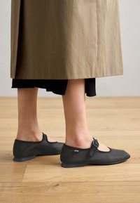 Scarpe Mary Jane nere con tomaia in rete, suola piatta in gomma e fibbia laterale. Il design presenta una punta arrotondata e dettagli minimi.