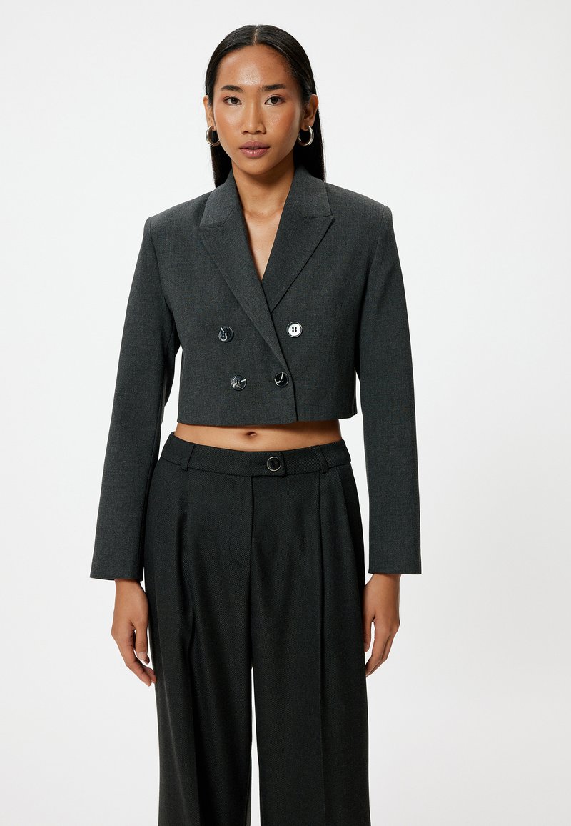 Blazer gris de corte corto, de doble botón, con mangas largas y botones negros, combinado con pantalones de pierna ancha grises de cintura alta.