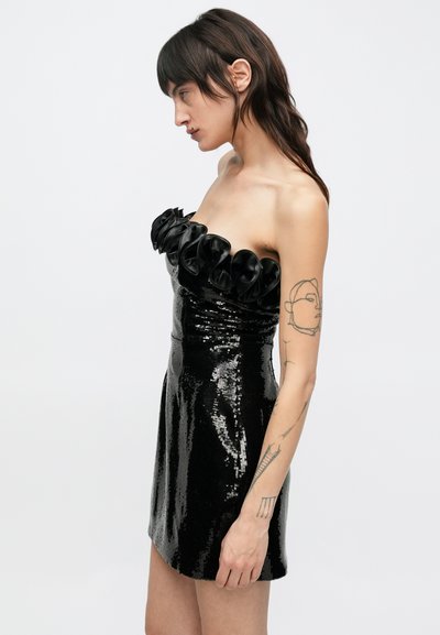 Melna kleita ar spīdīgiem fliteriem, pieguloša dizaina, bez siksnām un ar volānu dekorāciju ap kaklu. Gluda tekstūra un spīdīga virsma.