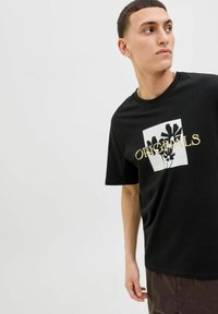 Camiseta de algodón negra de manga corta con un gráfico cuadrado blanco y un diseño floral, acentuada con texto dorado que dice "ORIGINALS."