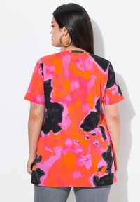 Tričeko s krátkým rukávem se živým tie-dye vzorem v odstínech růžové, oranžové a černé, vyrobené z měkké, texturované tkaniny.