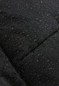 Tessuto nero resistente all'acqua con una superficie testurizzata, caratterizzato da gocce d'acqua. Design trapuntato con linee di cucitura visibili.