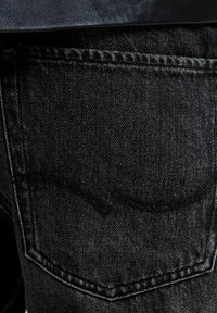 Jeans de mezclilla negra que presentan un diseño de bolsillo trasero característico con costura distintiva. La textura del material tiene un ligero desgastado, lo que enfatiza su durabilidad.