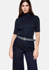 Marineblauwe coltrui met korte mouwen, gecombineerd met donkere spijkerbroek met brede pijpen en een contrasterende geruite riem met een zilveren gesp.