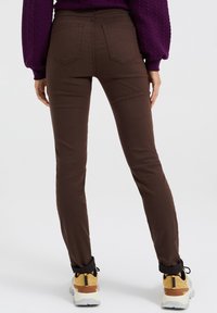 Ruske skinny hlače z gladko teksturo, z dvema zadnjima žepoma in prilegnjeno obliko. V kombinaciji z rumenimi in sivimi športnimi copati.