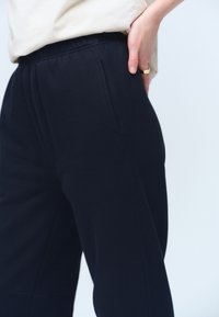 Laivastonsiniset rentomalliset collegehousut pehmeästä materiaalista, joissa on joustava vyötärönauha ja sivutaskut, sileällä tekstuurilla.