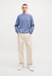 Suéter de tricot texturizado azul claro com decote arredondado, combinado com calças largas bege e ténis brancos. Complimentos visíveis.