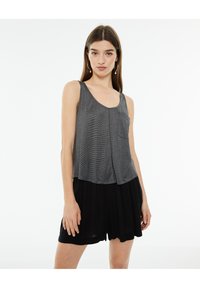 Top gris sin mangas con un escote en forma de arroba, cuenta con un bolsillo en el pecho y una silueta fluida, combinado con pantalones cortos sueltos negros. Textura de tela suave.