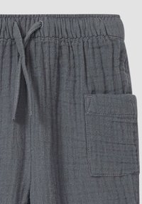 Grau melierte, strukturierte Hosen mit elastischem Bund und Zugband, ausgestattet mit einer Seitentasche und einem rautenförmigen Muster für zusätzliche Details.