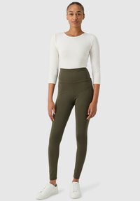 Leggings taille haute vert olive en tissu extensible, associés à un haut ajusté à manches longues blanc et à des baskets blanches.