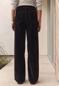 Pantalones anchos de pana negra con cintura alta, que cuentan con dos bolsillos traseros, textura suave y diseño recto.