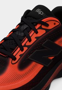 Sort og knall oransje treningssko med sorte lisser, mesh-tunge merket "ellipse" og en stor svart logo på siden.