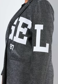 Silbergraues Blazer mit strukturierter Oberfläche. Verfügt über ein schwarz-weißes Druckdesign mit Text. Enthält eine Tasche an der Seite.