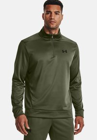 Grüner Sportpullover aus glattem, feuchtigkeitsableitendem Material. Mit einem Viertelreißverschluss-Kragen und einem schwarzen Logo auf der linken Brust.