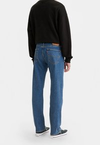 Jeans de mezclilla azul con un corte recto relajado, que presentan una etiqueta de cuero en la parte trasera y bolsillos con costuras distintivas. Sudadera negra recortada.