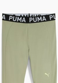 Jasnozielone spodnie sportowe z czarnym pasem, na którym widnieje napis "PUMA" w białym kolorze. Gładka faktura, dopasowany krój i boczne szwy.