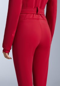 Piros kezeslábas, testhez simuló sziluettel, bordázott derékrésszel és hosszú ujjakkal. Az anyag simának és rugalmasnak tűnik.