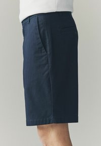 Marineblaue Baumwollshorts mit geradem Schnitt, seitlichen Taschen und einer Gesäßtasche mit Knopfverschluss. Glatte Textur, knielanges Design.