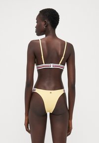 Gul bikini med tunna justerbara axelband och en flerfärgad rand. Har en minimal design och en klassisk skärning nertill.