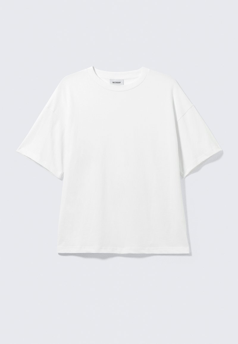 Weißes oversized T-Shirt mit kurzen Ärmeln und Rundhalsausschnitt mit eingesetzten Schultern, flach auf hellgrauem Hintergrund.