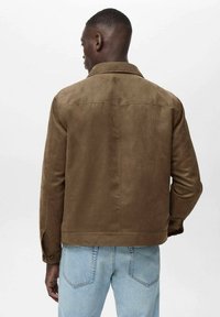 Veste en daim marron avec un col classique, couture de dos, et poignets boutonnés, associée à un jean en denim bleu clair.