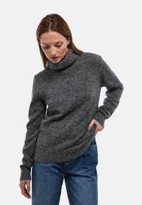 Pull à col roulé gris en tissu doux et texturé avec manches longues, coupe décontractée, et détails côtelés aux poignets et à l'ourlet, porté avec un jean bleu.