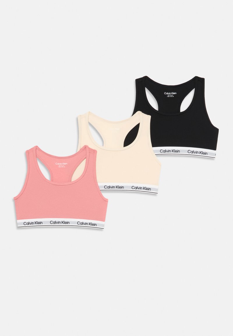 Trzy sportowe biustonosze Calvin Klein w kolorach różowym, beżowym i czarnym, z białymi elastycznymi paskami z logo Calvin Klein.