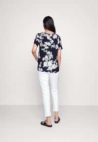 Hladký vršek s květinovým vzorem v námořnické modři, krátké rukávy a kulatý výstřih, doplněný bílými kalhotami a černými klouzavými botami. Hladká textilie.