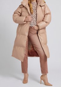 Lång, puffy jacka i ljusrosa med hög krage och tryckknappar. Bärs över en mönstrad tröja och rosa jeans, kompletterad med nude-hälar.