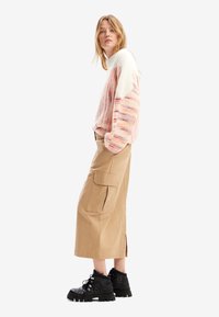 Strikket genser med rosa og hvite striper, paired med khaki cargo skjørt som har sidelommer og splittkant. Svarte snørebånd støvler fullfører looken.