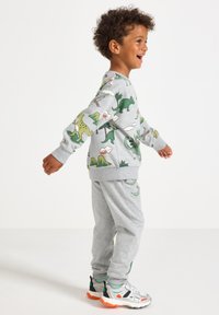 Gray children's tracksuit with dinosaur prints, featuring long sleeves and elastic cuffs, paired with gray sweatpants and colorful sneakers.