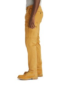 Gula cargobyxor med sidfickor, med en rak ben-design och synlig sömnad. Bärs med matchande gula stövlar.