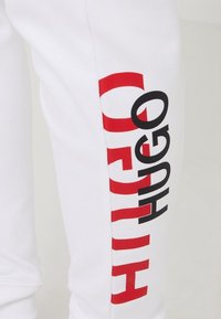 Witte joggingbroek met een gedurfde rode en zwarte "HUGO" grafische print langs het linkerbeen. Zacht, katoenen materiaal met een aansluitend ontwerp.