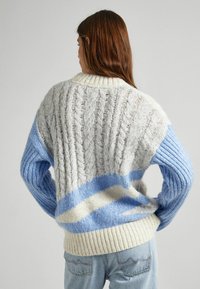 Paksu neulepusero, jossa on lankavahva neulontamalli harmaan, vaaleansinisen ja kerman värissä; siinä on resorit hihansuissa ja helmassa, väljällä istuvuudella ja kontrastivärisillä osioilla.