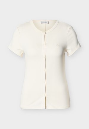 Rövid ujjú krémszínű, gombos ing kerek nyakkivágással és apró, mellkasra hímezett logóval.