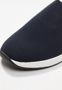 Marinblå mesh slip-on-sko med en texturerad yta, som har en vit mellansula och en rund gummiyttersula.