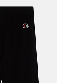 Black cotton joggers with an elastic waistband, featuring a small embroidered logo in red and white on the left thigh.