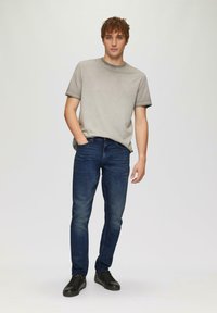 Camiseta gris de cuello redondo, jeans oscuros ajustados y zapatillas negras. Diseño simple con una textura suave y un minimalismo en los detalles.