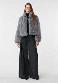 Szara, sztuczna futrzana kurtka o krótkim kroju z wysokim kołnierzem i szerokimi rękawami, zestawiona z szerokimi, ciemnymi spodniami. Gładka tekstura, brak widocznych elementów metalowych.