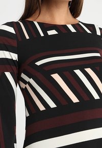 Black long-sleeve top featuring a geometric pattern of wide and narrow stripes in burgundy, white, and soft pink. Rounded neckline.