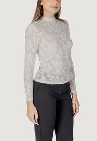 Top a maniche lunghe in pizzo bianco con motivi floreali; materiale morbido e trasparente; colletto alto; abbinato a pantaloni neri su misura.