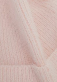 Světlá růžová pletenina s texturovaným, načechraným povrchem. Má vertikální žebrování a měkké, nadýchané okraje.