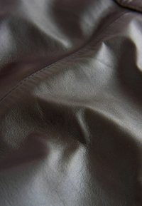 Tessuto in pelle marrone con una superficie liscia e texture che mostra lievi pieghe, cuciture e lucentezza, a indicare un materiale di alta qualità.