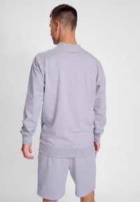 Felpa grigia chiara con maniche lunghe e polsini a costine, abbinata a pantaloni corti dello stesso colore. Il tessuto sembra morbido e ha un taglio casual.