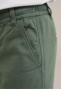 Gröna bomullsblandade shorts med en slät textur, som har en sidoficka och stickade detaljer längs midjebandet och sömmarna.